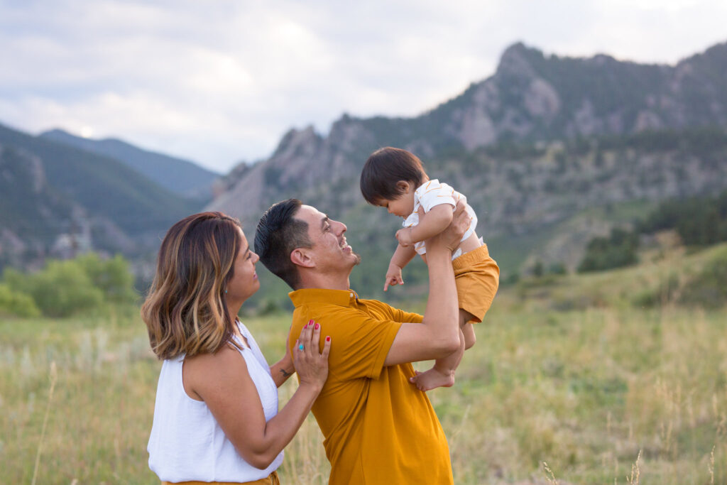 A father holds his baby up while mom smiles at the child. Taken by Stephanie Eddy, Boulder Photographer
