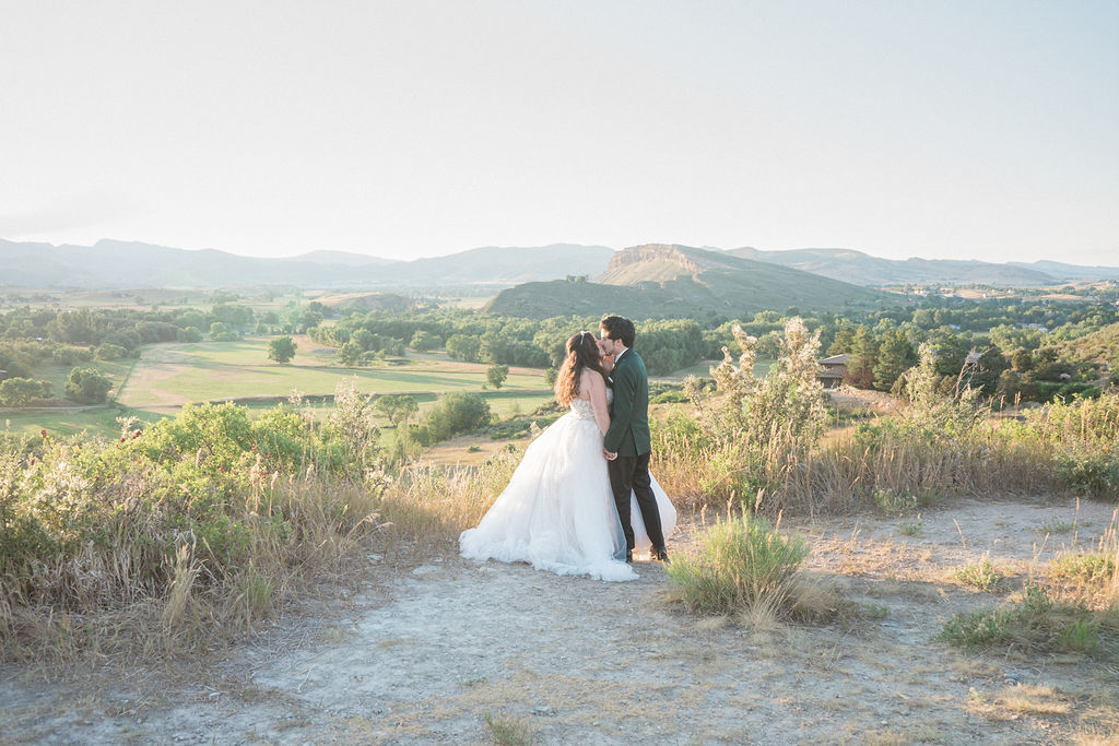 Newlyweds share a kiss on a bluff overlook at sunset holding hands at one of the Fort Collins Wedding Venues