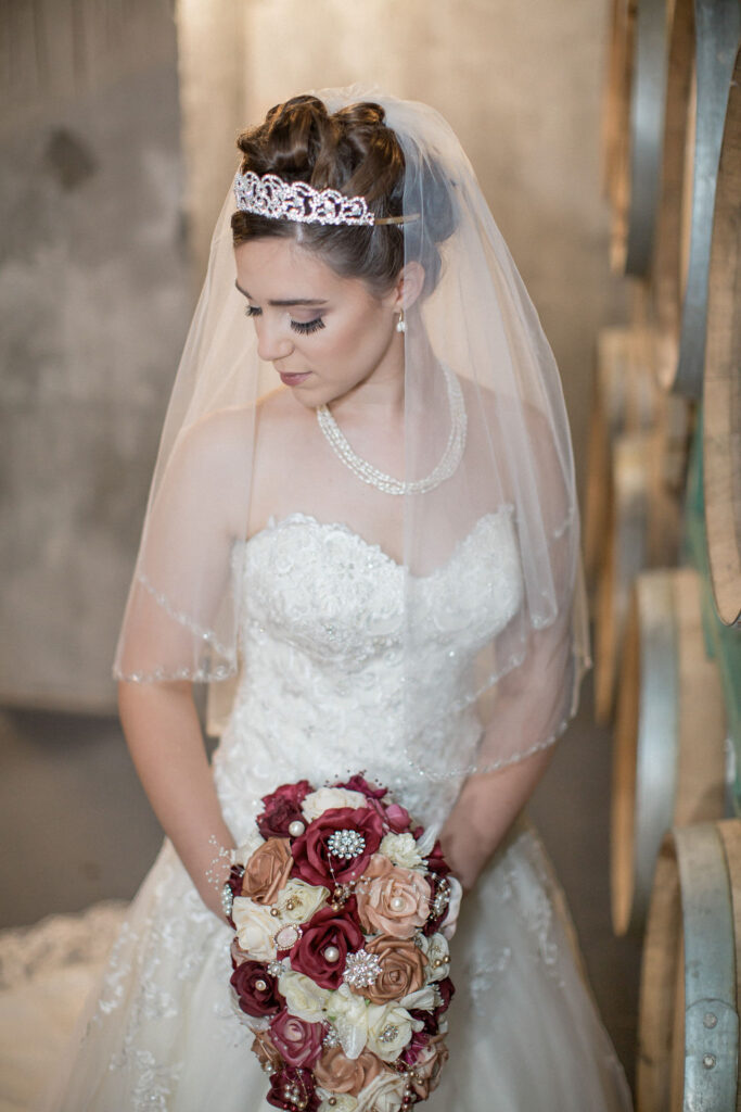A bride gazes down her shoulder in an elegant gown and veil holding a jewelry covered bouquet