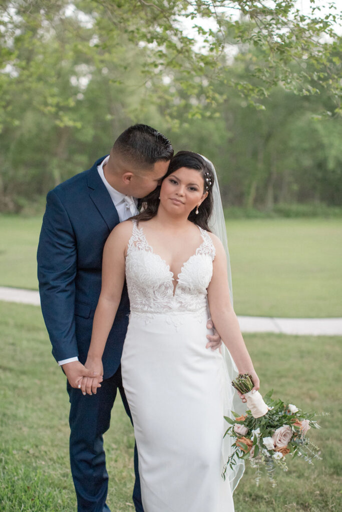 A bride lans into her groom as he kisses her cheek in a lawn at one of the Fort Collins Wedding Venues