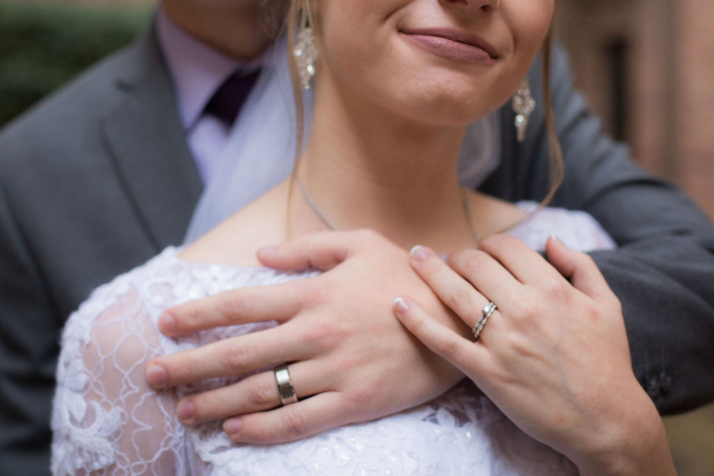 Details of a woman holding the arm of her groom over her chest with ring hands at Strauss Cabin Farmhouse