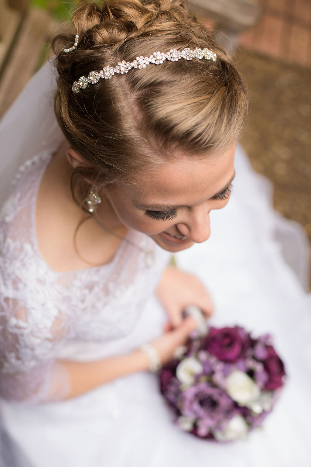 A look down at a bride sitting with her purple bouquet in her lap and diamond flower hairpiece in her hair at a Strauss Cabin Farmhouse wedding