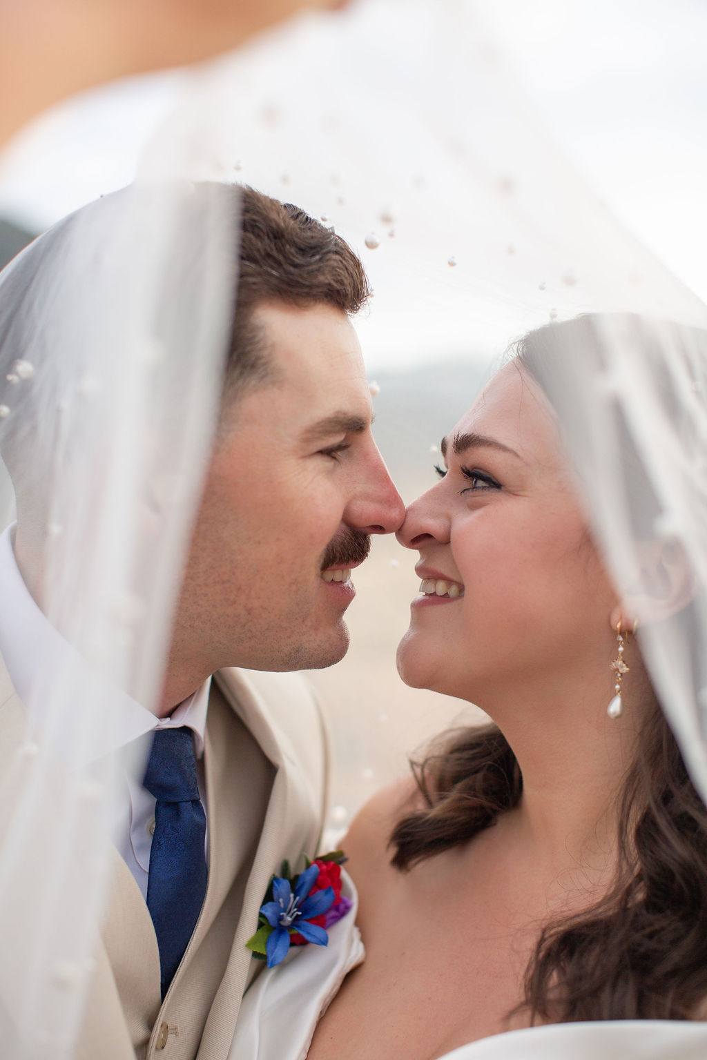 A bride and groom boop noses while hiding under the veil at their boulder sunrise amphitheater wedding