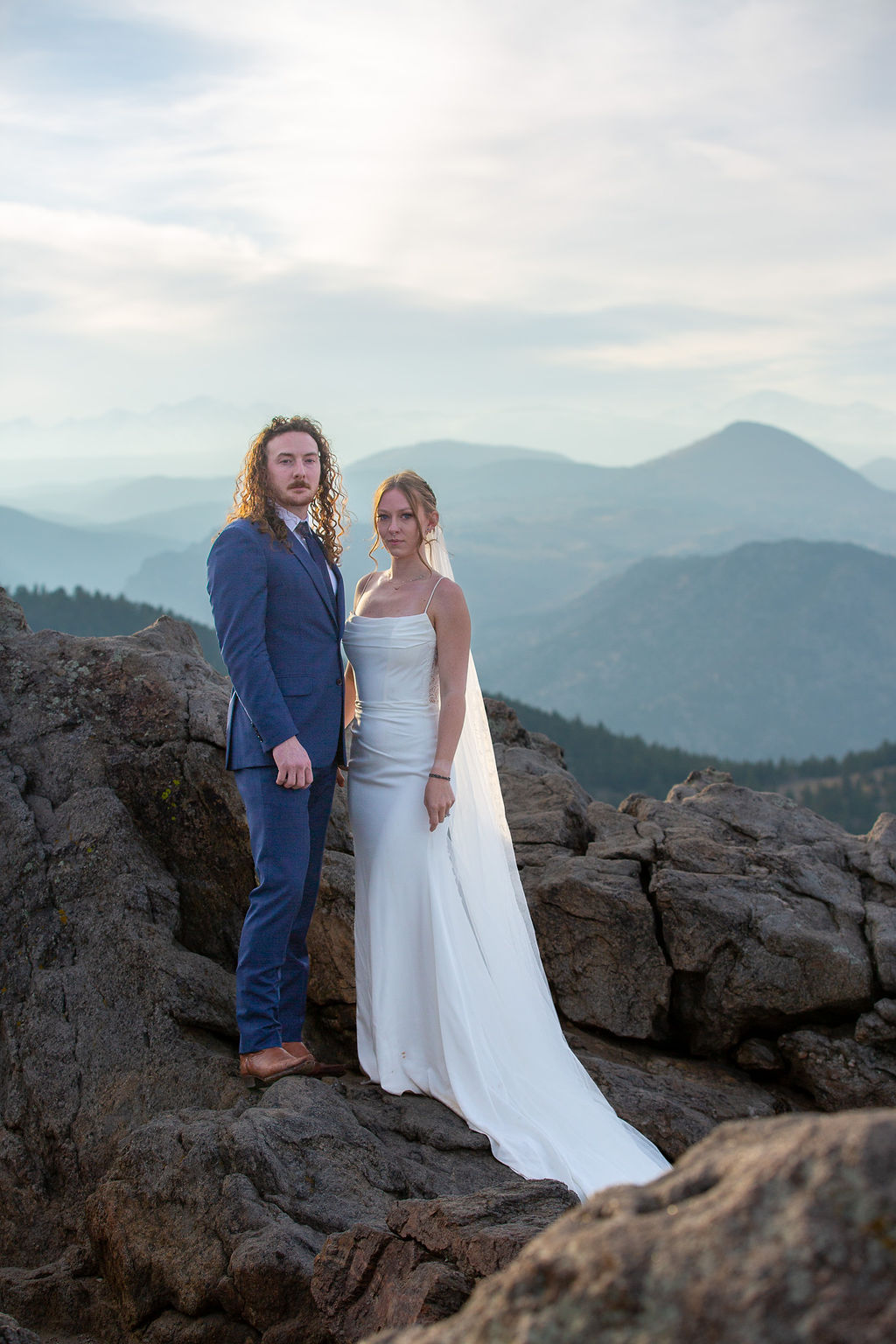 Newlyweds hold hands while standing in the rocky mountains at sunset