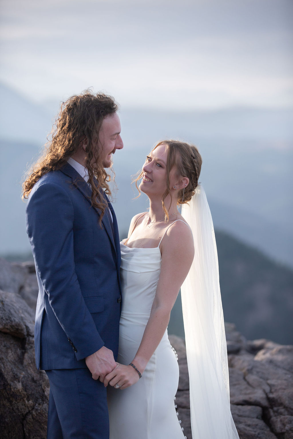 A bride and groom dance while smiling at each other in the mountains at sunset