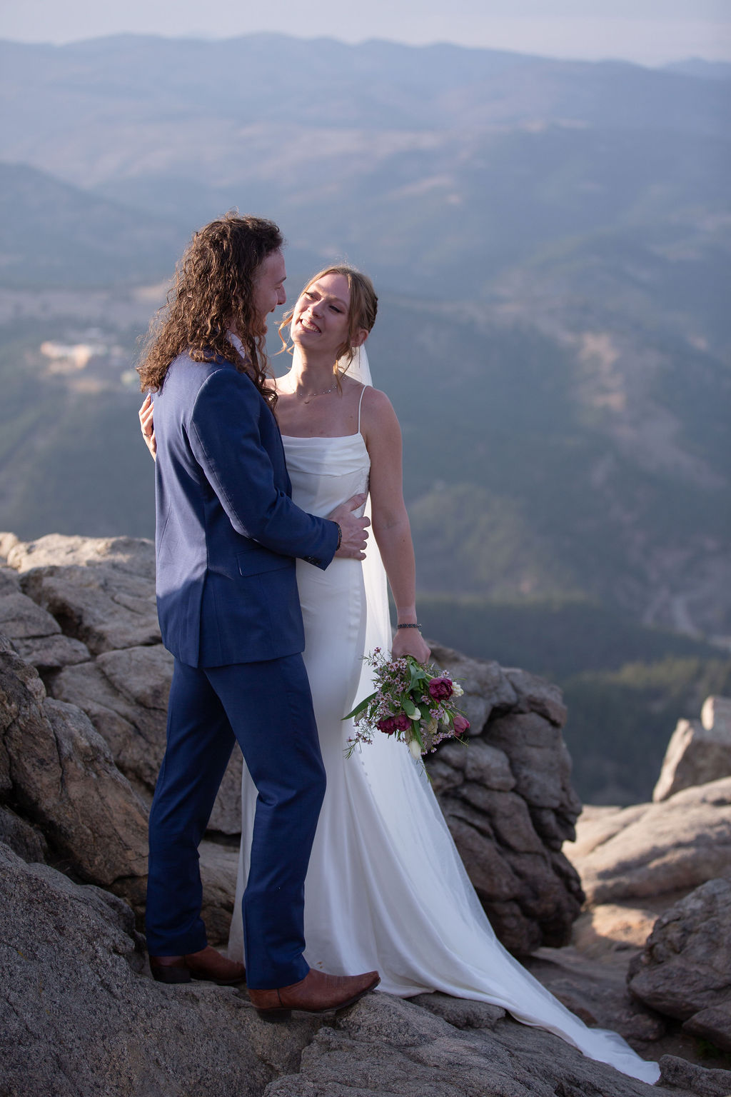 Newlyweds embrace and laugh while on a rocky mountain overlook at sunset