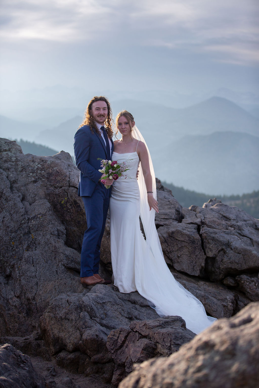 A bride and groom laugh while standing in a rocky overlook at sunset when eloping in boulder