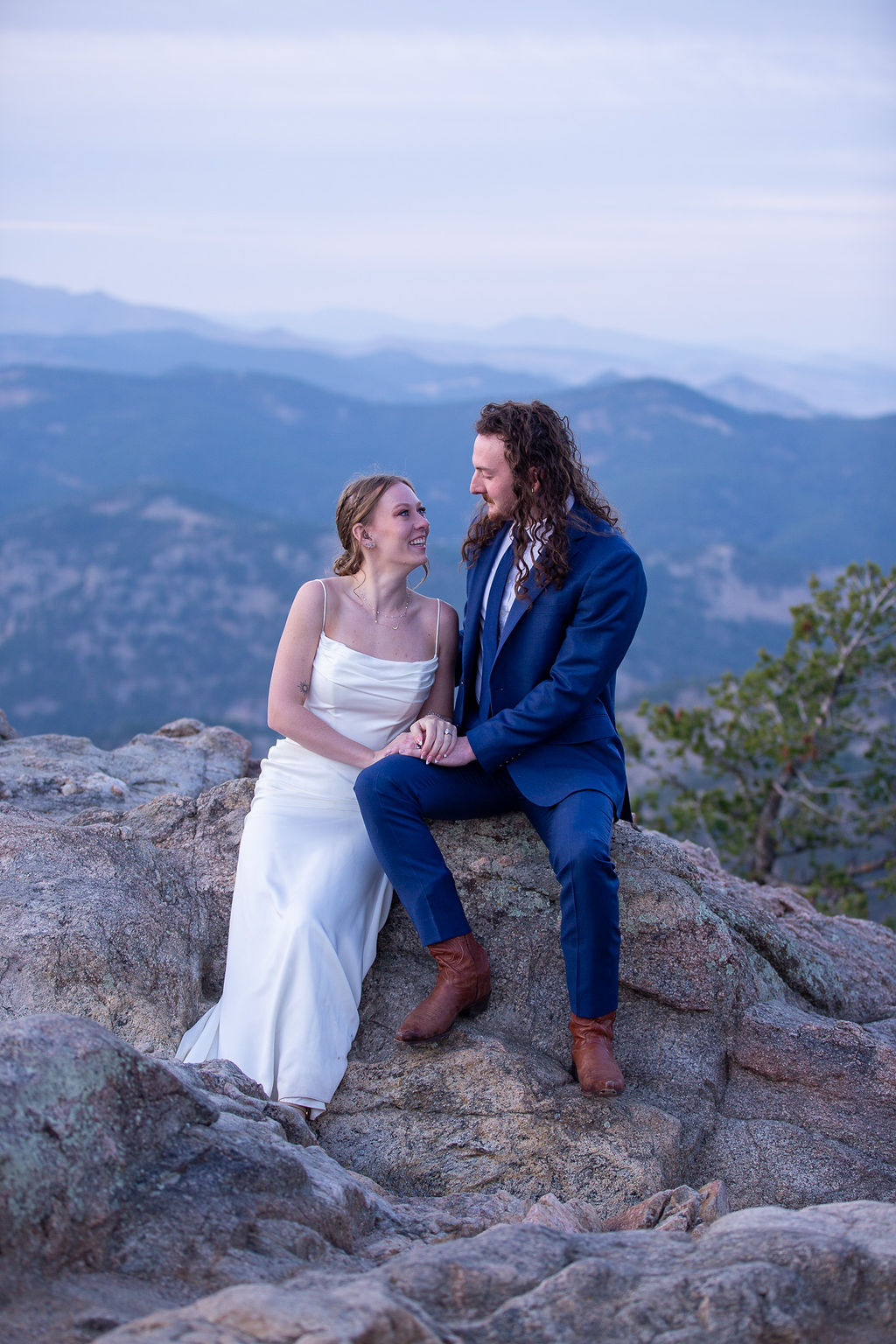 A bride and groom sit on a boulder on an overlook after a wedding hike while eloping in boulder