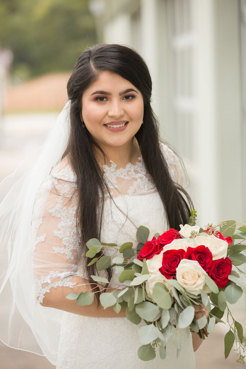A bride smiles in her lace gown while holding a red and white bouquet at her greenbriar inn wedding