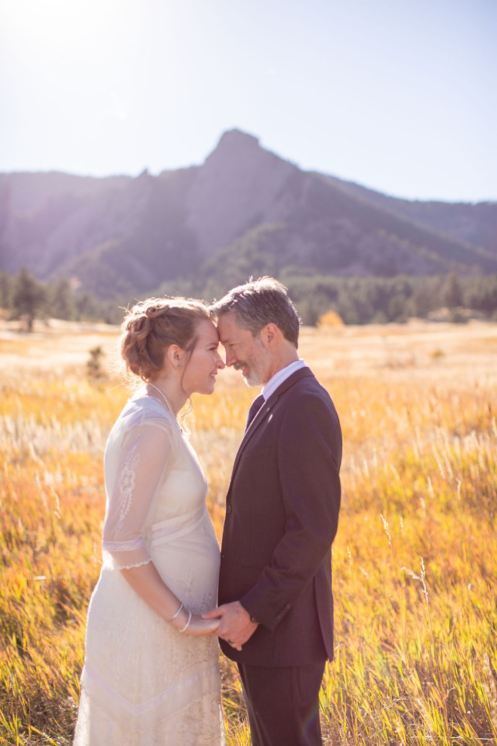 Happy newlyweds touch foreheads while holding hands in a field of tall golden grass