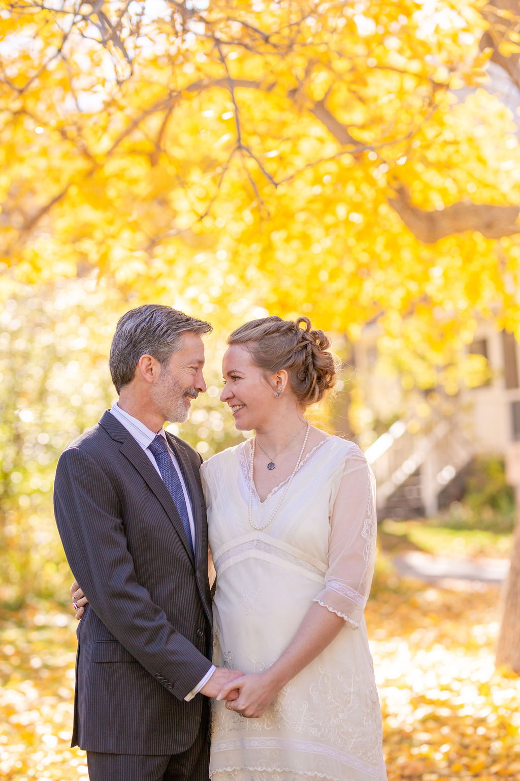 A bride and groom stand under a golden tree holding hands and smiling at each other during their rembrandt yard wedding