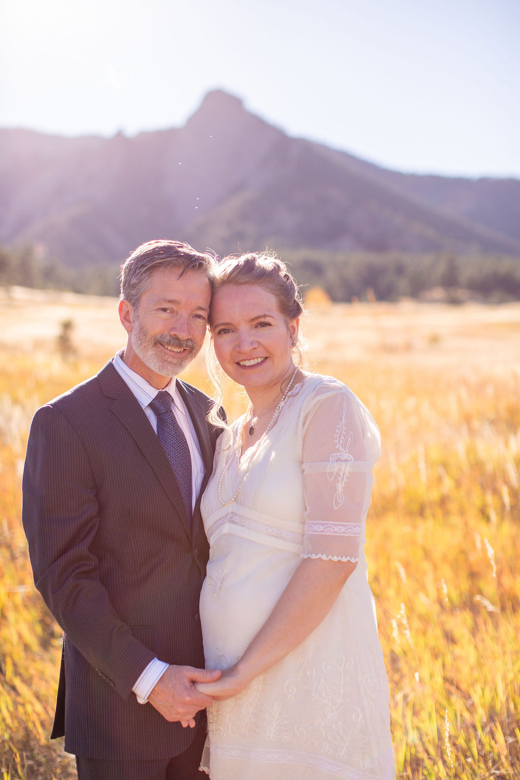 Happy newlyweds stand touching foreheads in a field of gold grass at their rembrandt yard wedding