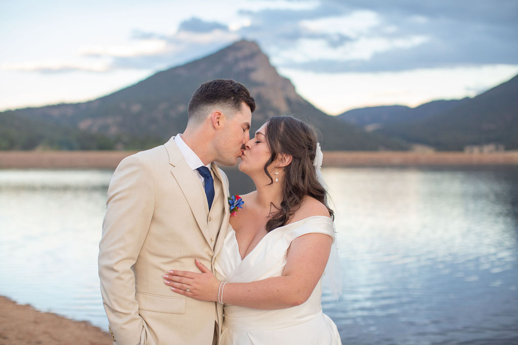 NEwlyweds kiss next to an alpine lake at sunset