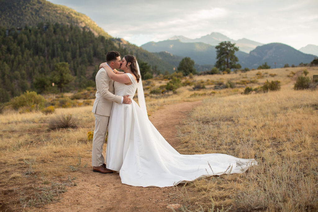 A bride and groom kiss in a mountain trail at sunset during their rocky mountain national park elopement