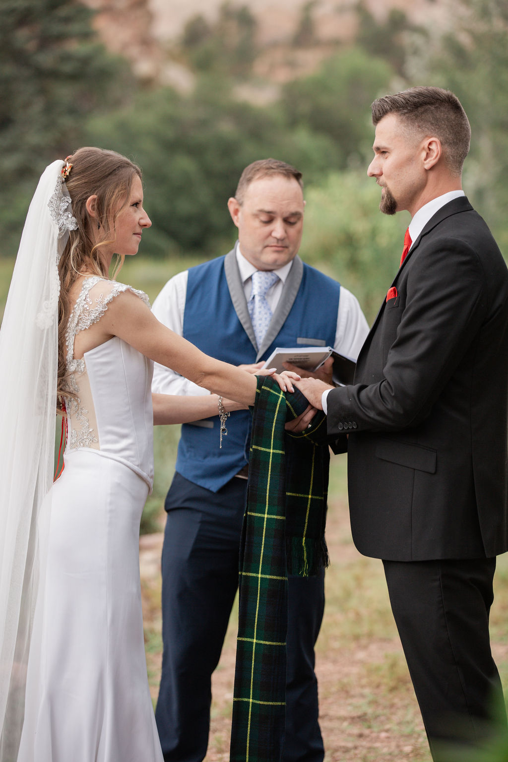 A bride and groom hold hands tied in a scarf as guided byt heir officiant during an outdoor ceremony