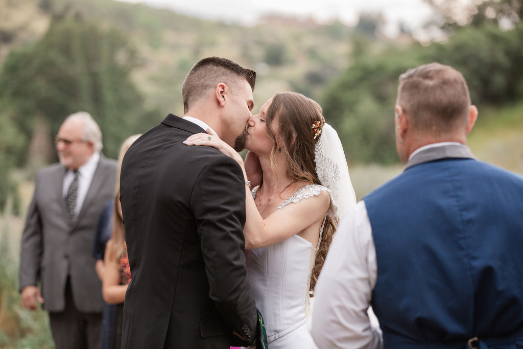 Newlyweds kiss to end their outdoor ceremony as guests watch during their romantic riversong inn wedding