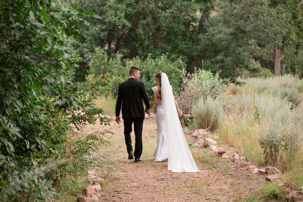 A bride and groom walk holding hands on a garden path and chatting during their romantic riversong inn wedding