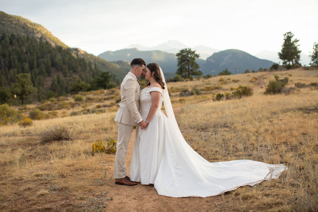 A bride and groom snuggle touching foreheads at sunset holding hands in the mountains