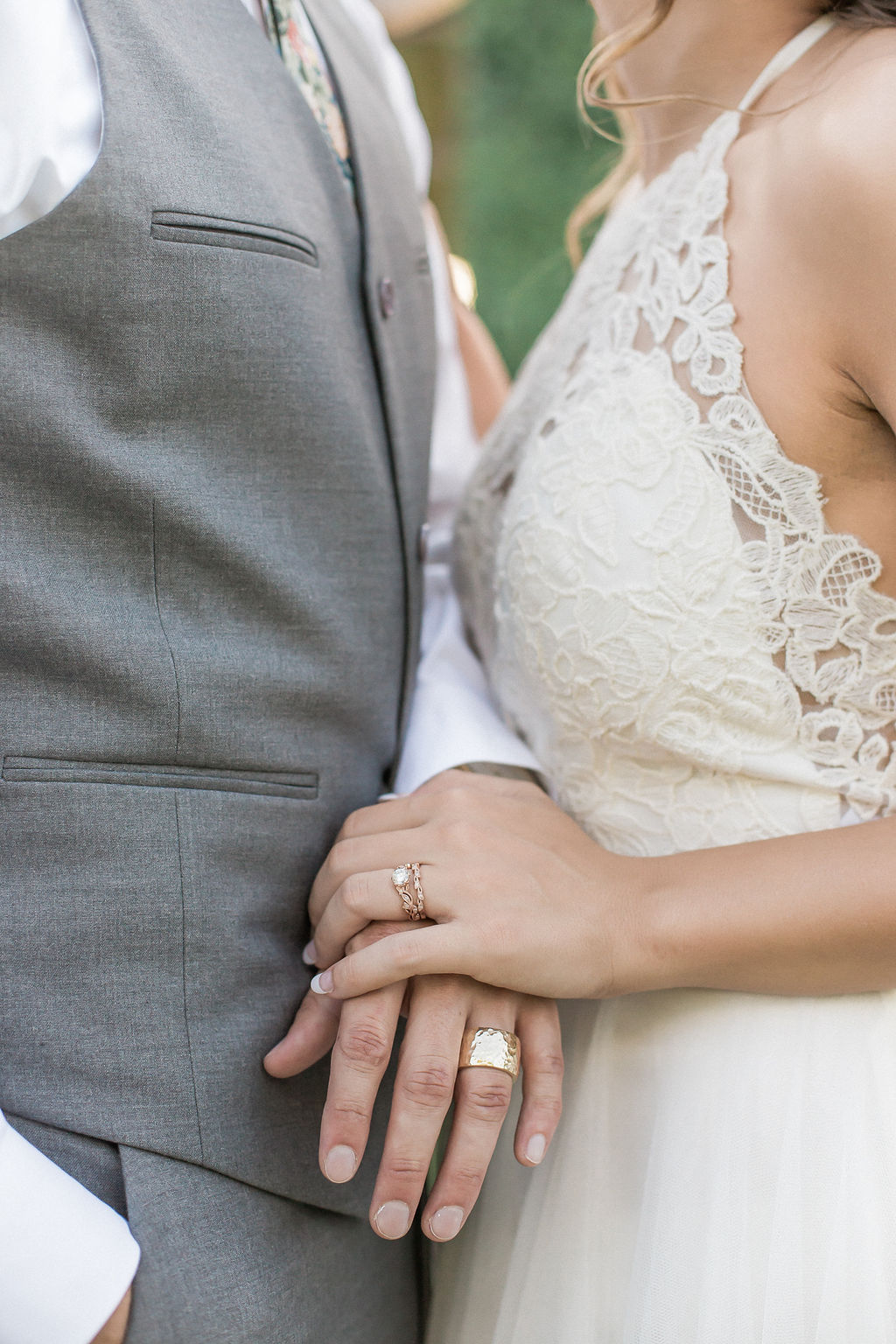 Details of newlyweds holding hands between them with rings against a lace gown at the mill event venue