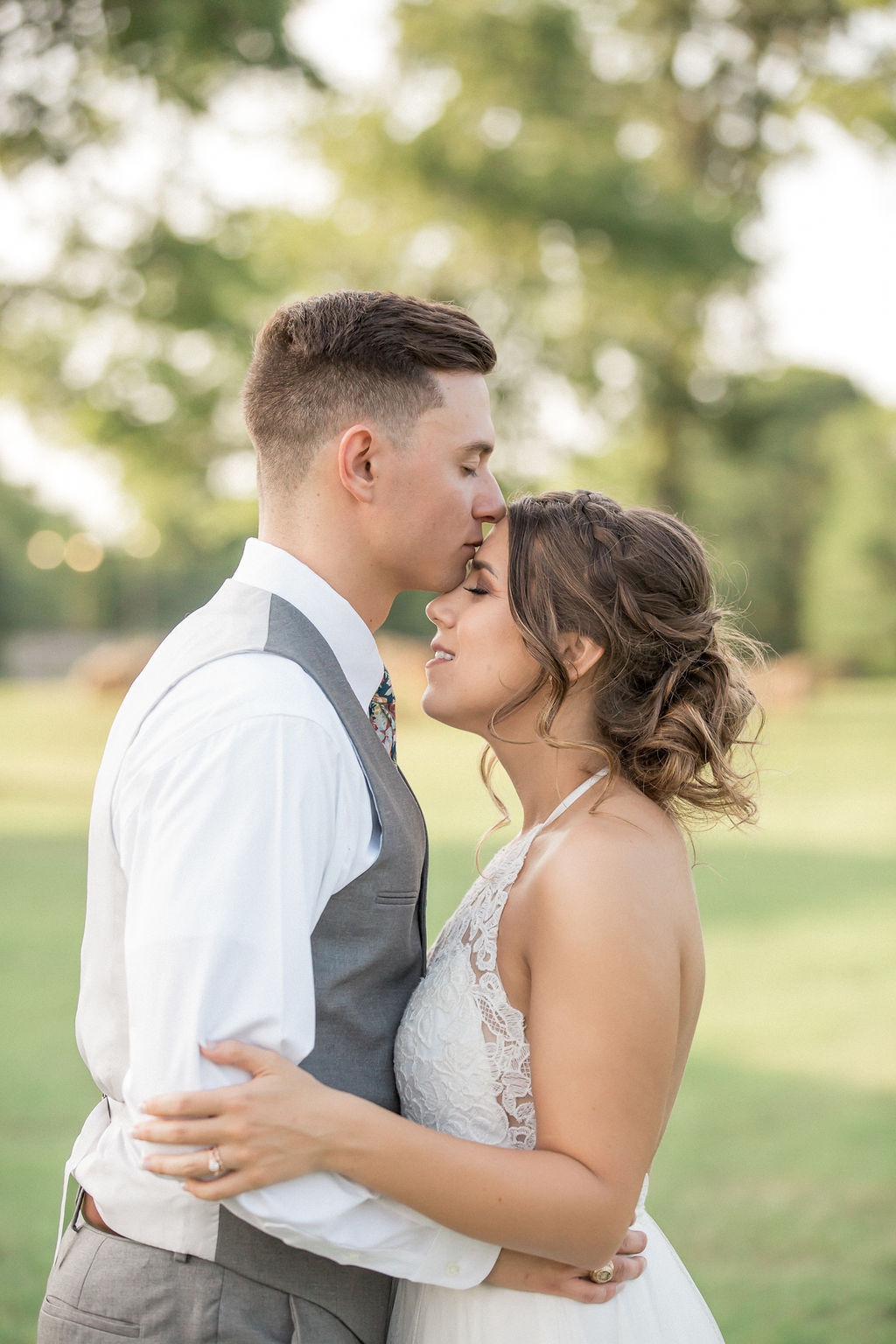 A groom kisses the forehead of his bride as they embrace in a garden
