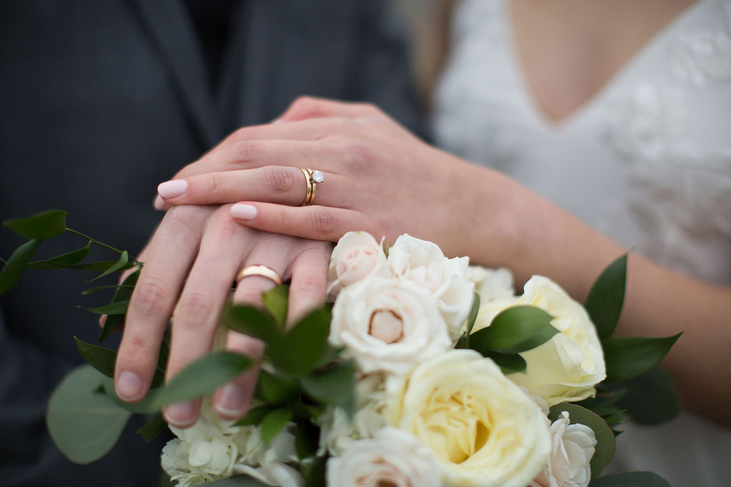 Newlyweds hold hands over a white rose bouquet with ring hands during their brookside gardens wedding