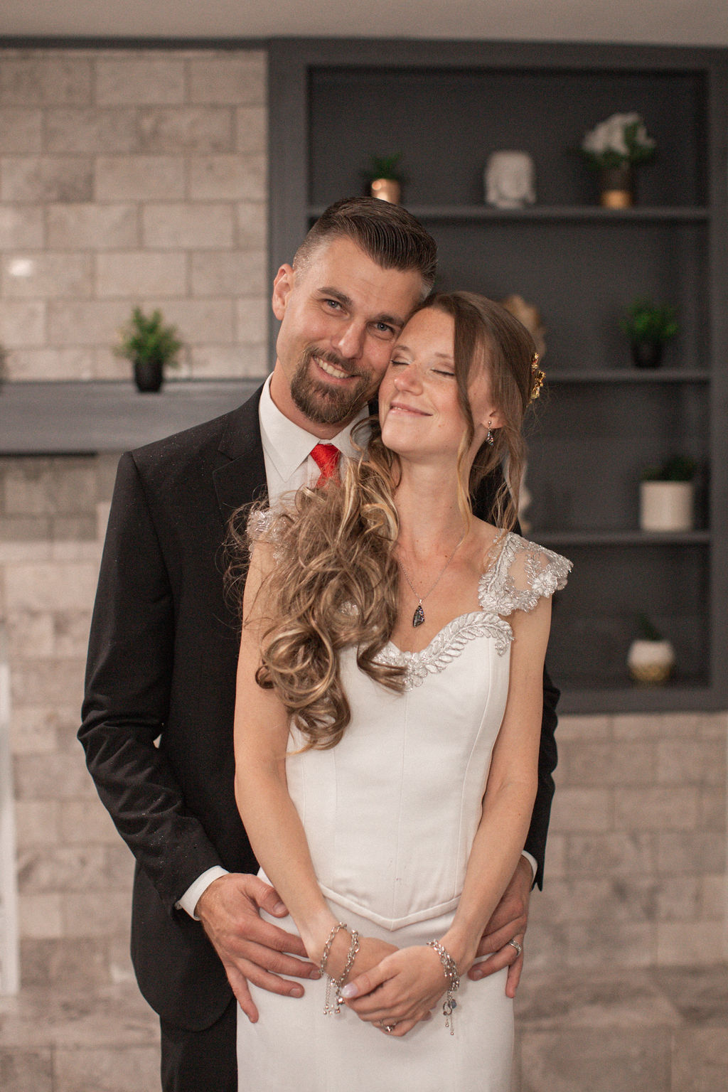Happy newlyweds snuggle and smile cheek to cheek in a brick room
