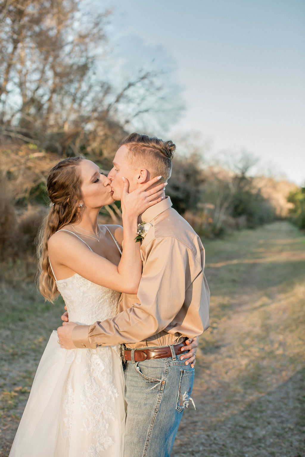 Newlyweds kiss while standing in a trail at sunset and holding each other