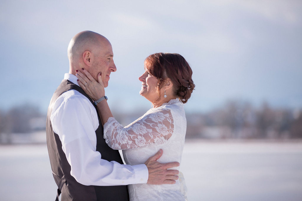 Newlyweds smile at each other with hands on hip and cheek at sunset while they elope in Estes Park