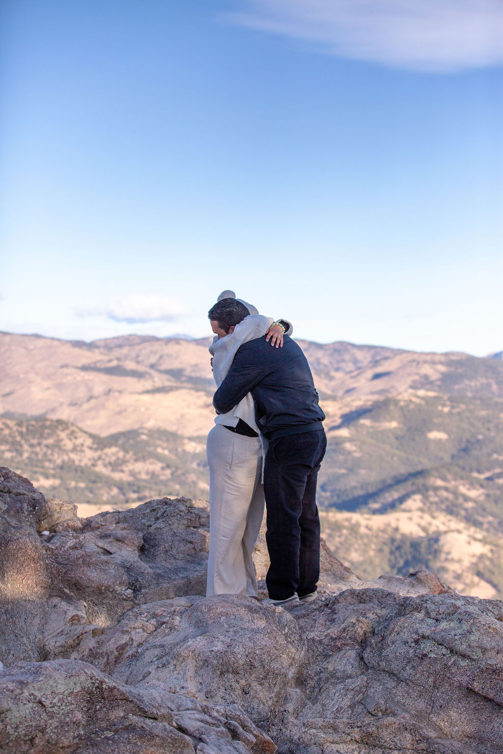 A newly engaged couple embraces on a mountain overlook after a hike at sunrise at one of the estes park elopement locations