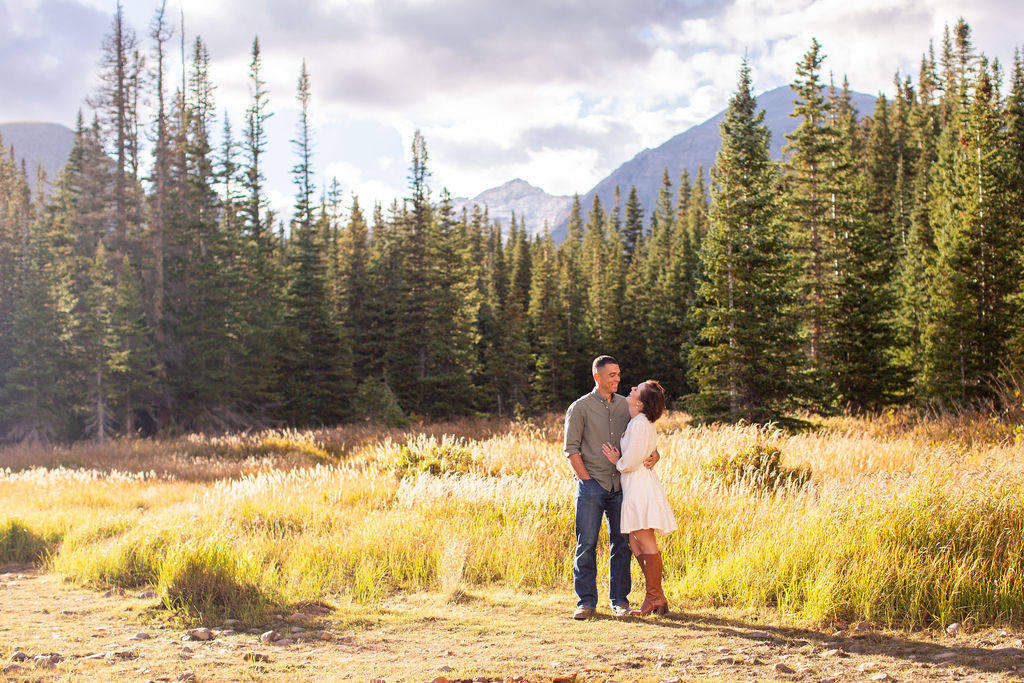 A happy couple embrace in a remote mountain trail in a white dress and green shirt