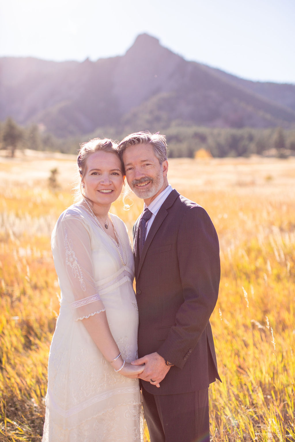 A happy newly married couple stand holding hands in a meadow of tall golden grass during their intimate wedding in colorado touching heads