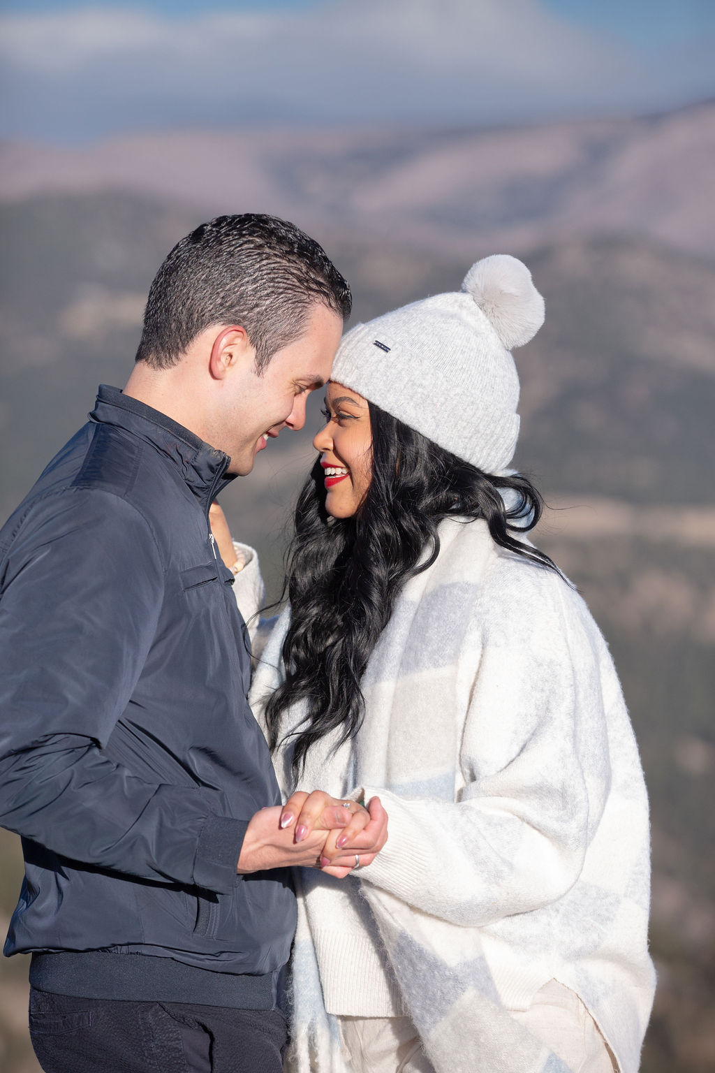 Happy newly engaged couple touch foreheads while smiling in the mountains and holding hands before needing a micro-wedding planner colorado