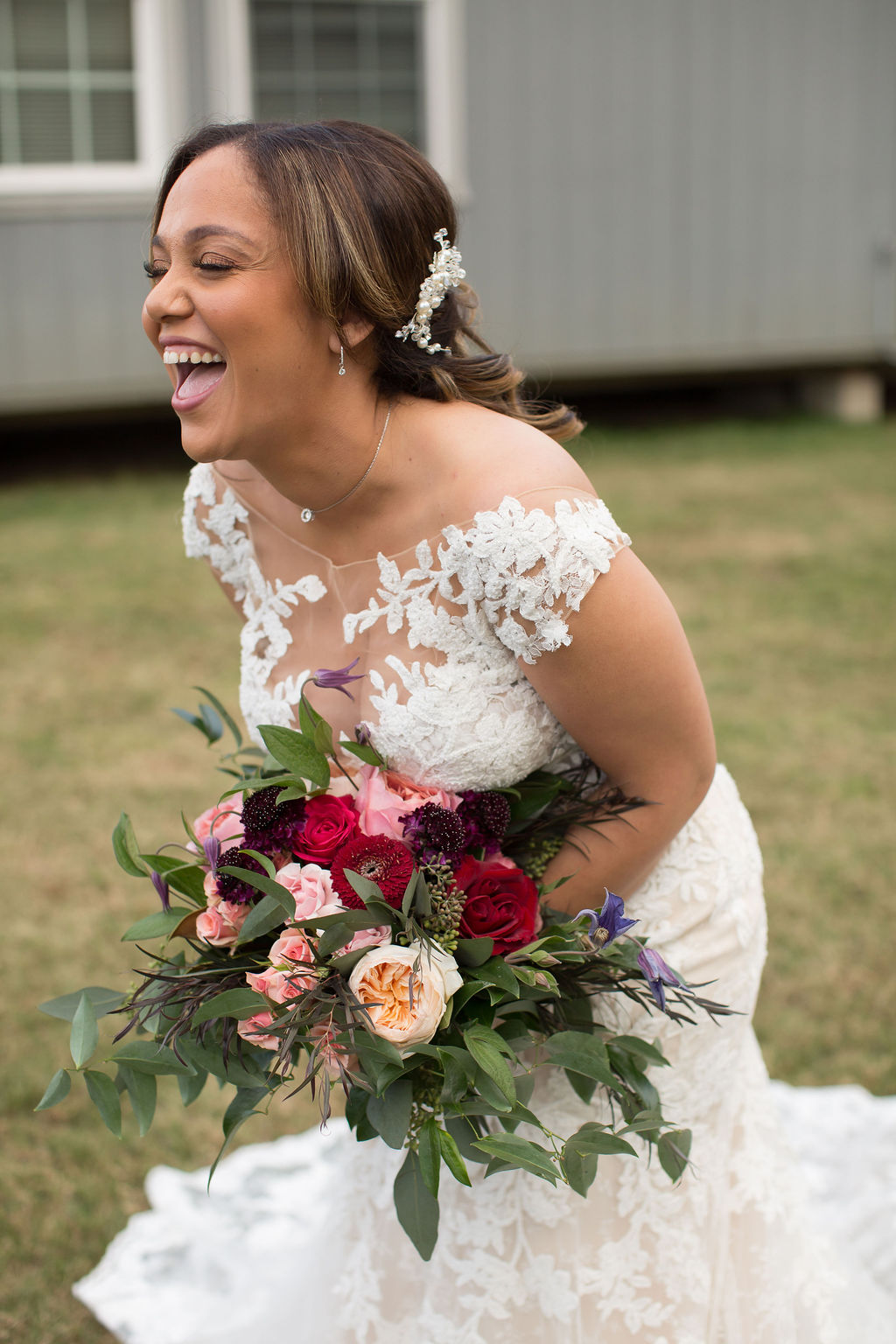 A bride laughs hard in her lace gown in a lawn holding a large colorful bouquet at one of the small wedding venues in Boulder, CO