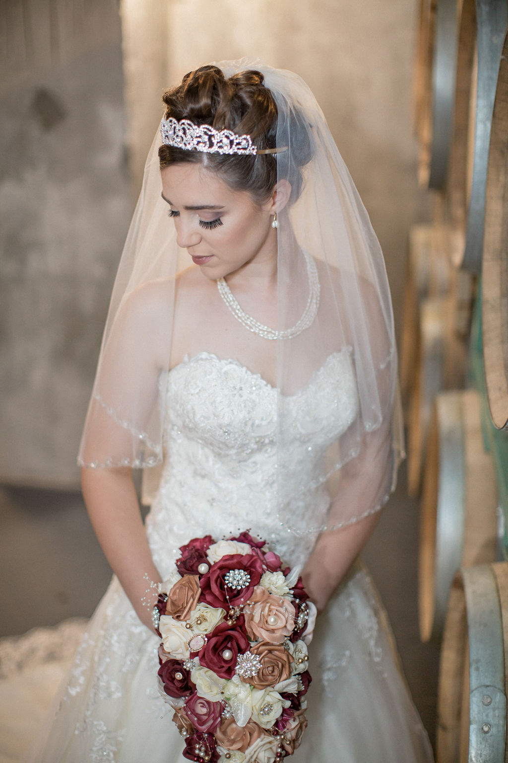 A bride gazes down her shoulder while standing in a barrel room holding her maroon and gold bouquet with a tiara at one of the small wedding venues in estes park