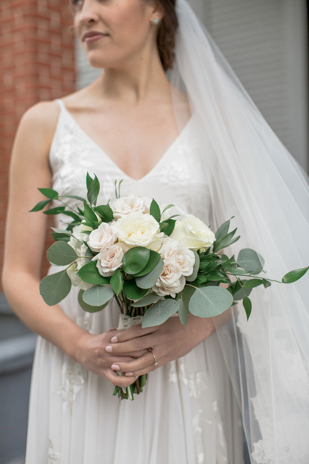 A happy bride stands holding her white rose bouquet outside at one of the wedding venues in Laporte, CO
