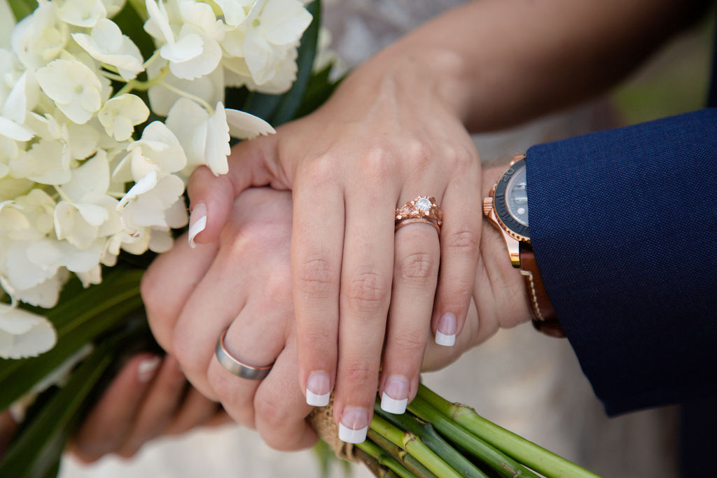 Details of newlyweds holding hands with ring hands on the white bouquet