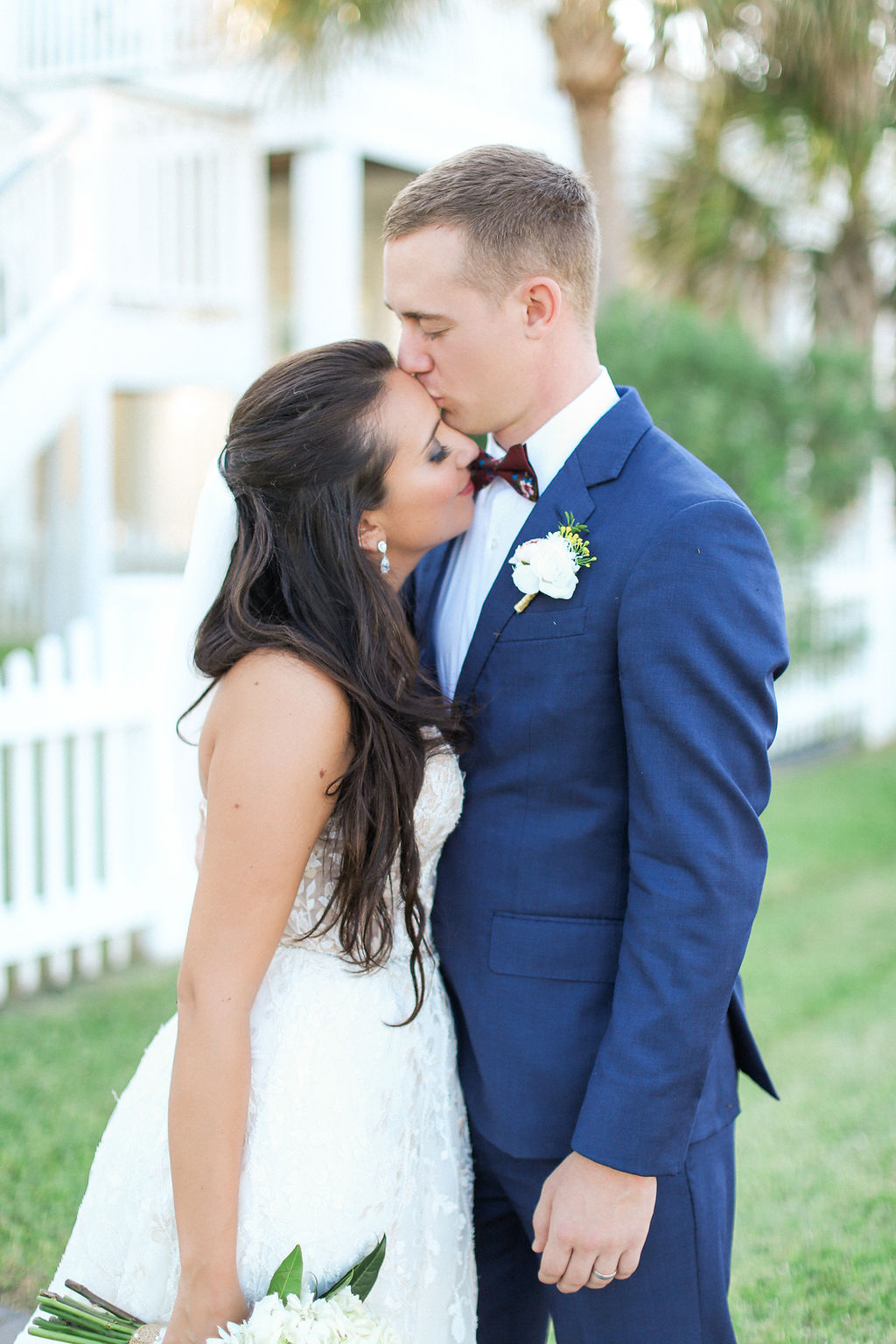 Newlyweds share a happy kiss while standing in a lawn in a blue suit and lace gown