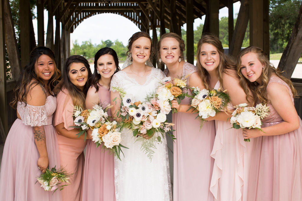 A bride smiles with her bridesmaids on a wooden covered bridge at one of the wedding venues in northern colorado