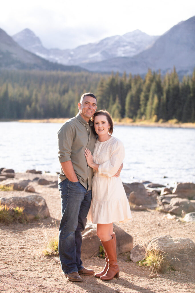 Newlywed couple holding each other beside a peaceful alpine lake in Rocky Mountain National Park.